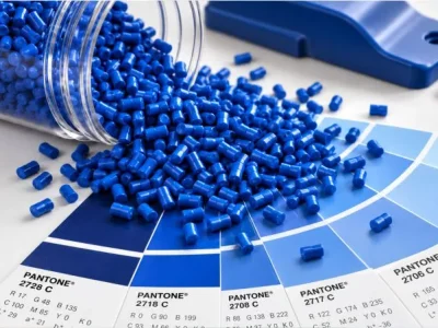 Peças plásticas em tons de azul com pellets de masterbatch sobre escala Pantone, representando o desenvolvimento de cor na indústria plástica