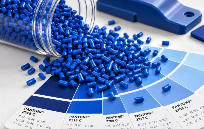Peças plásticas em tons de azul com pellets de masterbatch sobre escala Pantone, representando o desenvolvimento de cor na indústria plástica